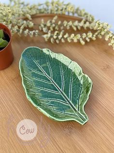 a green leaf shaped plate sitting on top of a wooden table next to a potted plant