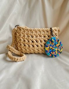 a crocheted purse with a blue ball hanging from it's side on a white background