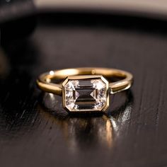 a ring with an emerald cut diamond on it sitting on top of a wooden table