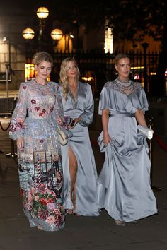 three women in long dresses are walking down the street at night, one is wearing a flowered dress