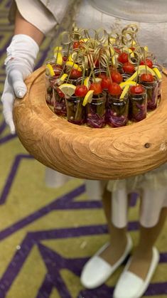 a person in white gloves holding a wooden platter filled with pickles and tomatoes