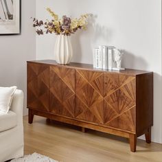 a vase with flowers sitting on top of a wooden cabinet next to a white couch