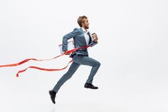 a man in a suit running with a red ribbon around his waist and holding a cup