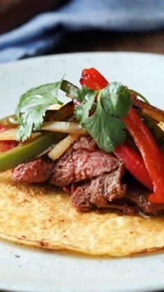 a white plate topped with meat and veggies on top of corn tortilla