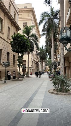 an empty city street with palm trees and people walking on the sidewalk in front of buildings