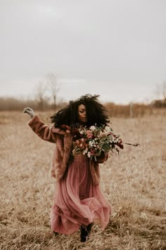 a woman in a pink dress and fur coat walking through a field