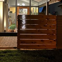 a wooden gate with numbers on it in front of a house at night, lit up by lights