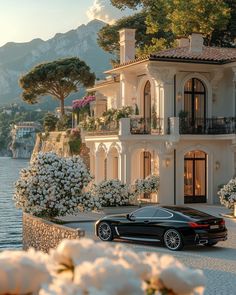 a black car parked in front of a large house next to the water and trees