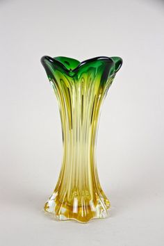 a yellow and green glass vase sitting on top of a white table next to a wall