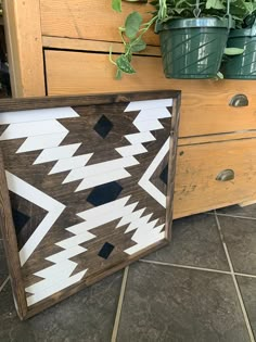 a wooden sign with black and white designs on it next to some potted plants