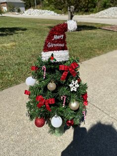 a small christmas tree on the sidewalk with ornaments around it and a santa hat on top