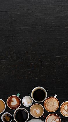 many different types of coffee are lined up on a black table with one cup in the middle