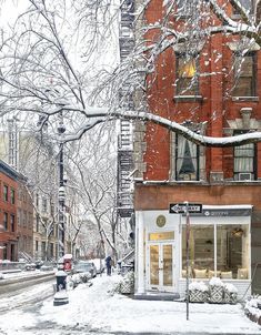 a snow covered street corner with people walking on the sidewalk and buildings in the background