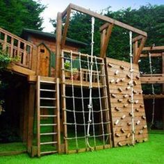 a wooden play structure with climbing ropes and ladders on the grass in front of trees