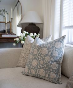 two pillows sitting on top of a couch next to a vase with flowers in it