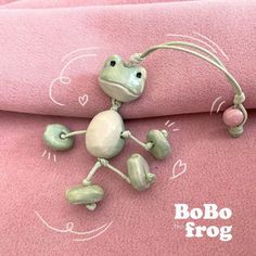 a small frog figurine is posed on a pink blanket with the word bobo frog written across it