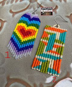 two colorful beaded earrings sitting next to each other on top of a cloth covered surface