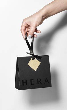 a hand holding a black bag with a tag on it that says hera hanging from the side