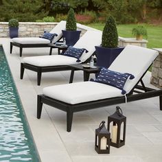 lounge chairs next to a swimming pool with lanterns on the ground and trees in the background