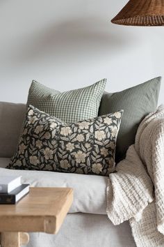 a couch with pillows on it next to a table and lamp in a room that has white walls