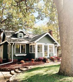 a green house with white trim on the front and side of it, surrounded by trees