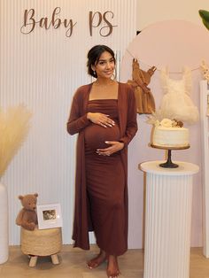 a pregnant woman standing in front of a baby shower sign and cake with her hand on her belly