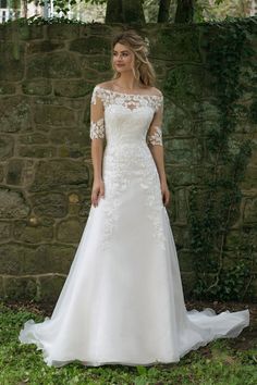 a woman in a white wedding dress standing next to a brick wall with her hands on her hips