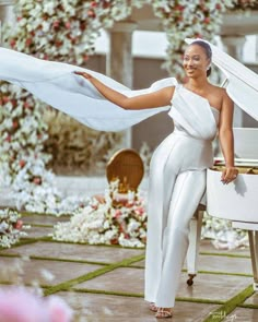 a woman in white is posing next to a grand piano and flowers on the ground