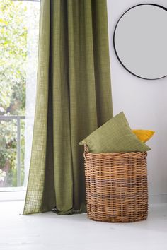 a wicker basket sitting next to a window with green drapes on the windowsill