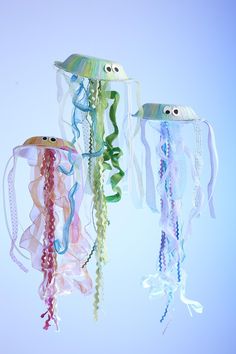 three jellyfishs are hanging from strings in the air with ribbons attached to them