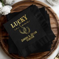 black napkins with gold lettering on them sitting on a wooden plate next to flowers