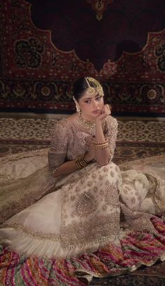 a woman sitting on top of a rug wearing a white dress and headdress