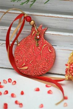 an ornament hanging from a red ribbon next to pomegranates