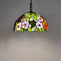 a stained glass lamp hanging from a chain on a gray wall with white and red flowers