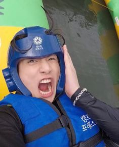 a woman in a life jacket is holding her hand up to her head while standing next to an inflatable raft