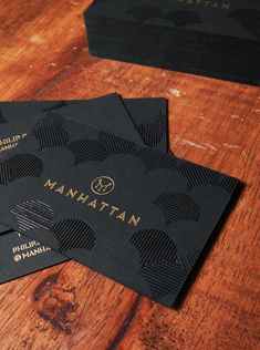 two black business cards sitting on top of a wooden table with gold foil logoing