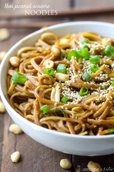 a white bowl filled with noodles topped with green onions and sesame seeds on top of a wooden table