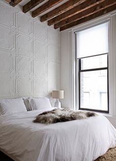 a white bed sitting next to a window in a room with wooden beams and a fur rug on top of it