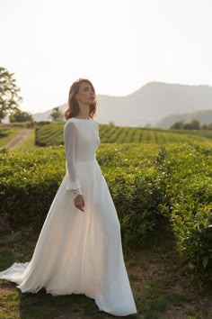 a woman in a long white dress standing on a field with mountains in the background