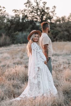 a man and woman holding hands in the middle of an open field with tall grass