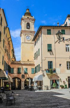 the clock tower is on top of an old building in this town square with tables, chairs and umbrellas