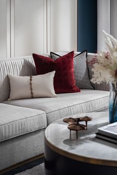 a white couch with red and black pillows sitting on it's side table next to a window