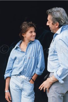 an older man standing next to a young woman in front of a black door with her hand on her hip