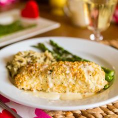 a white plate topped with chicken and asparagus covered in gravy next to a glass of wine