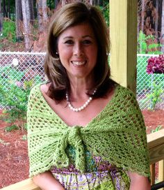 a woman standing on a porch wearing a green shawl and smiling at the camera