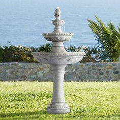 a water fountain in the middle of a grassy area next to a body of water