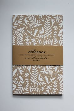 the notebook is printed with white leaves and has a brown paper label on it that says,