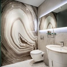 a white toilet sitting next to a sink in a bathroom under a large marble wall