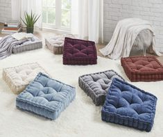 four different colored dog beds on a white rug