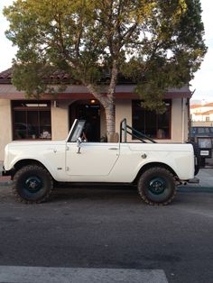 an old white truck parked in front of a building with a tree on the street